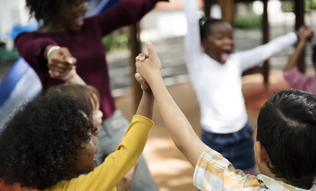 a group of diverse children holding hands and dancing and singing in a circle